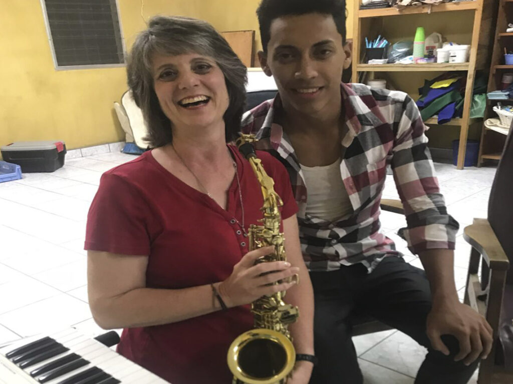 A woman and man holding a saxophone on top of a piano.