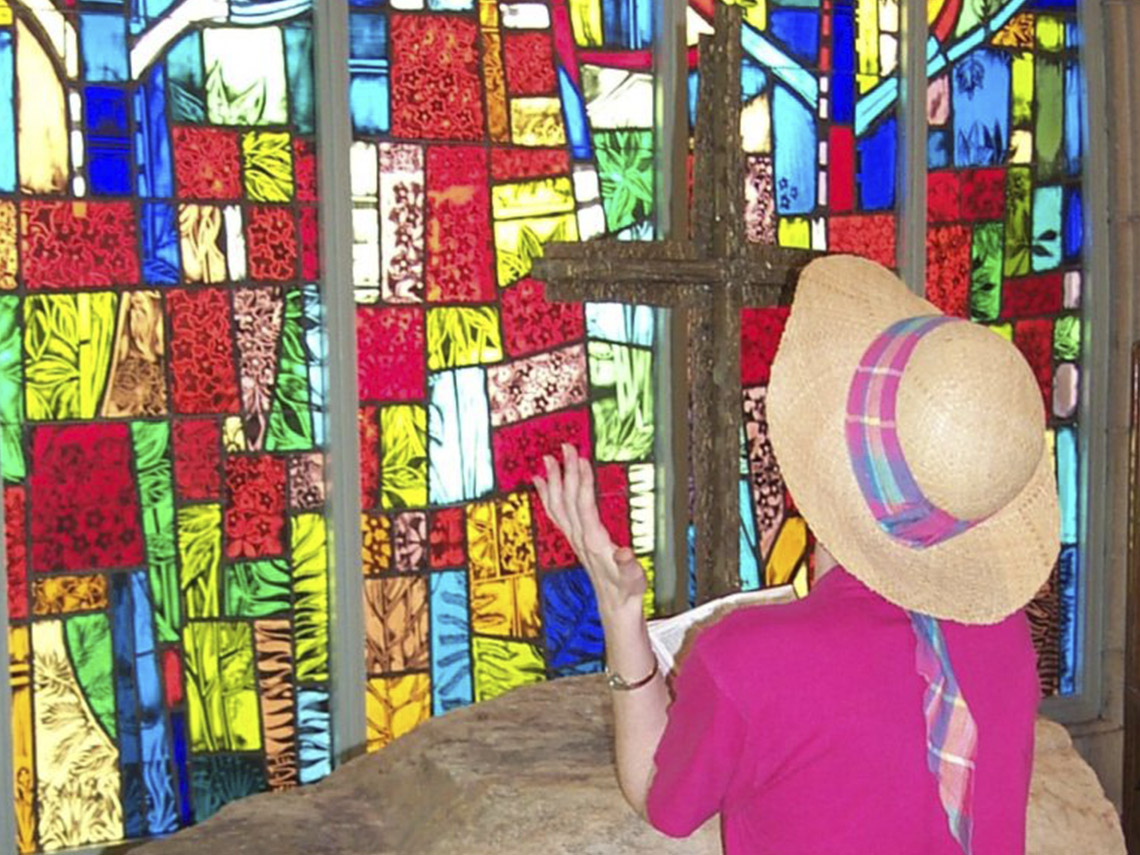 A woman in a straw hat standing next to stained glass.
