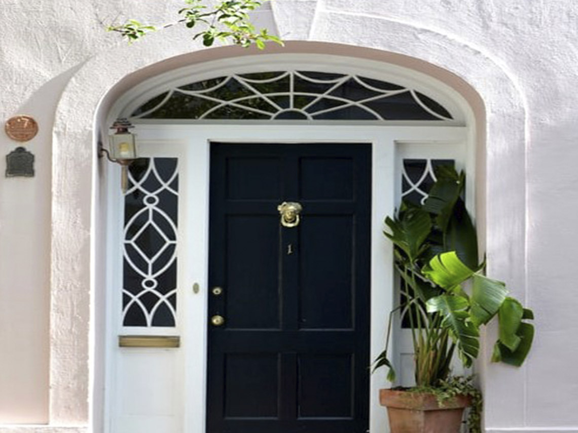 A black door with a white window and a plant in the corner.