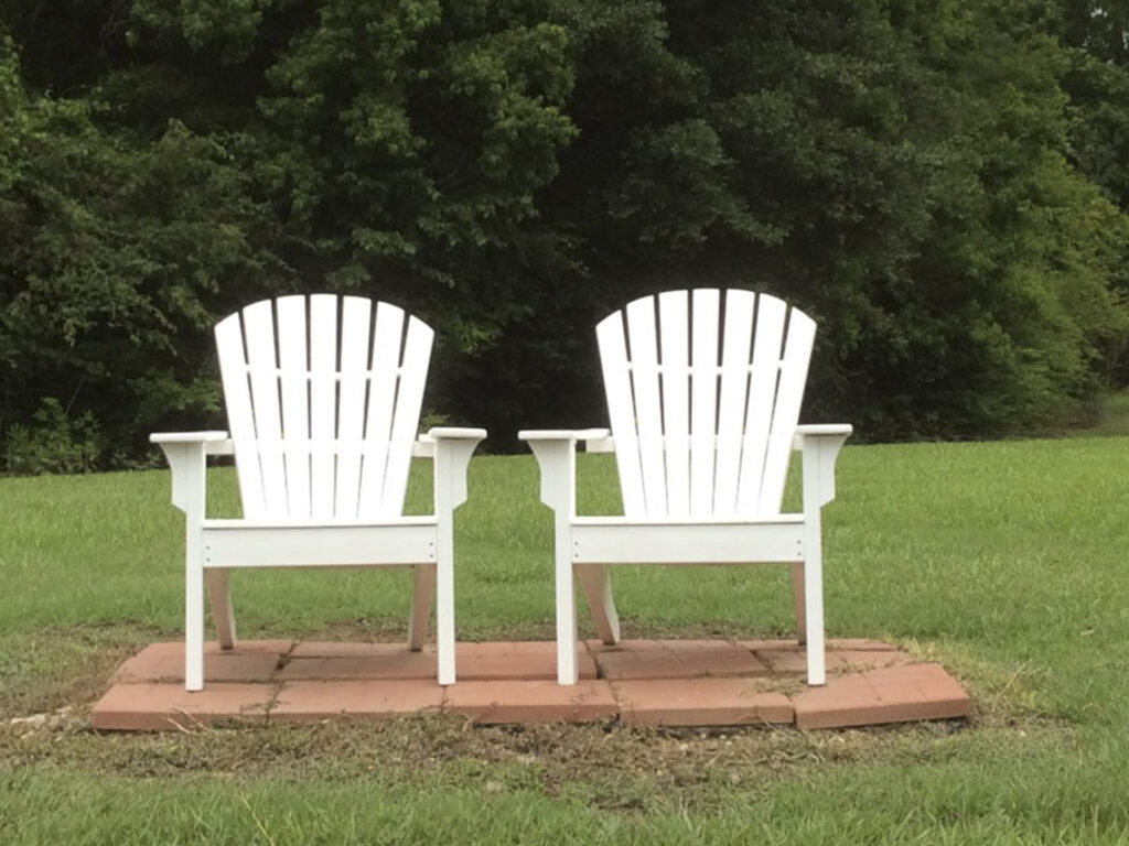 Two white lawn chairs sitting on a brick patio.
