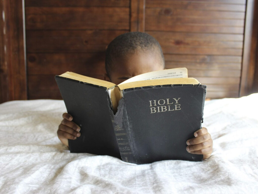 A young boy reading the bible on his bed.