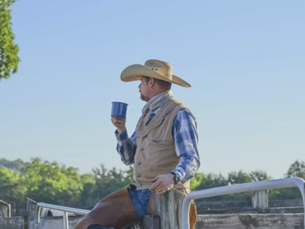 A man in cowboy hat holding a cup.