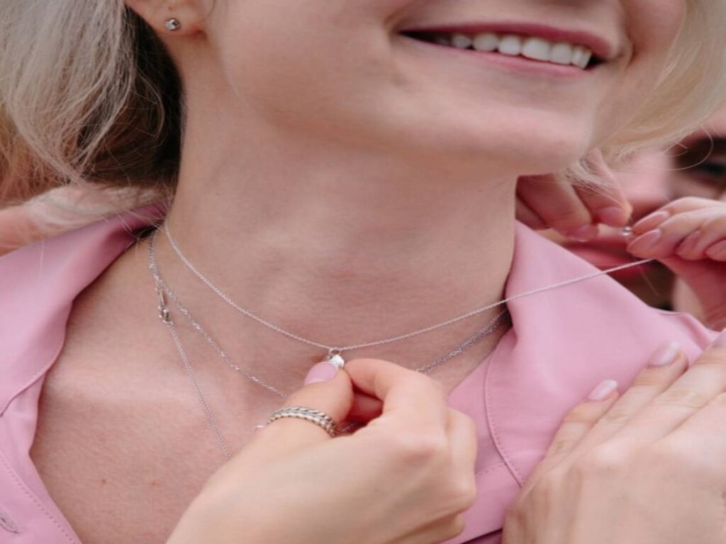 A woman wearing a pink shirt and holding onto her necklace
