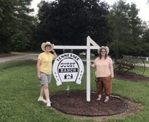 Two women standing next to a sign that says " tennessee trail guest ranch."