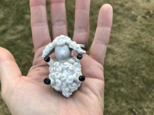 A hand holding a sheep figurine in the palm of its hand.