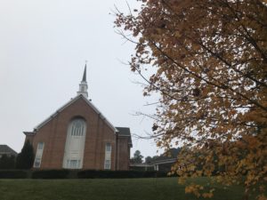 A church with a steeple and a tree in the foreground.