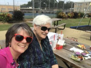 Two women sitting at a picnic table with food.