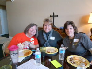 Three women sitting at a table with plates of food.