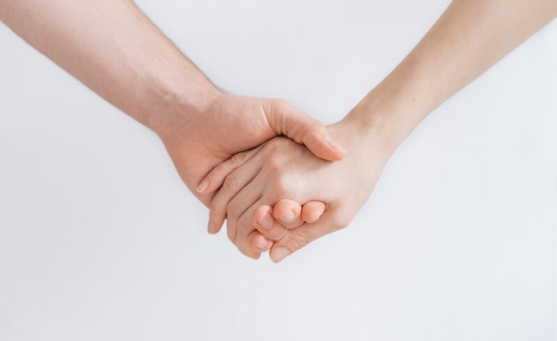 Two people holding hands in a white room.