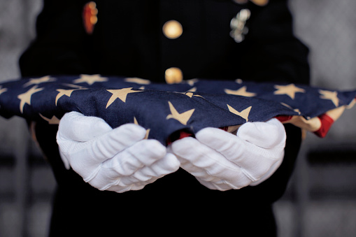 A person in white gloves holding an american flag.