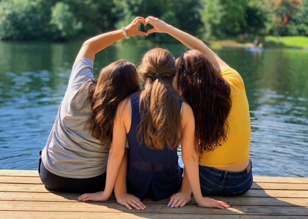 Three women sitting on a dock near the water.