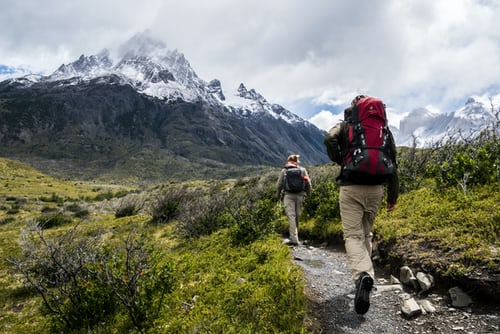 Two people walking on a trail in the mountains.