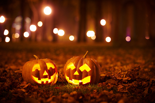 Two pumpkins with glowing faces sitting in the grass.
