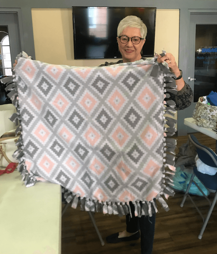 A woman holding up a blanket with pink and grey squares.