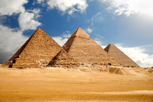Three pyramids in the desert under a blue sky.