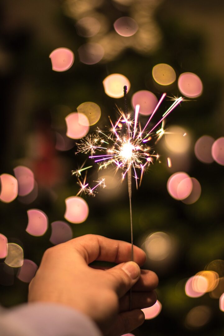 A person holding sparkler in front of blurry lights.
