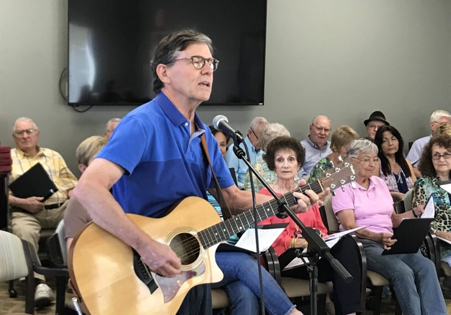 A man with glasses and a blue shirt is playing guitar