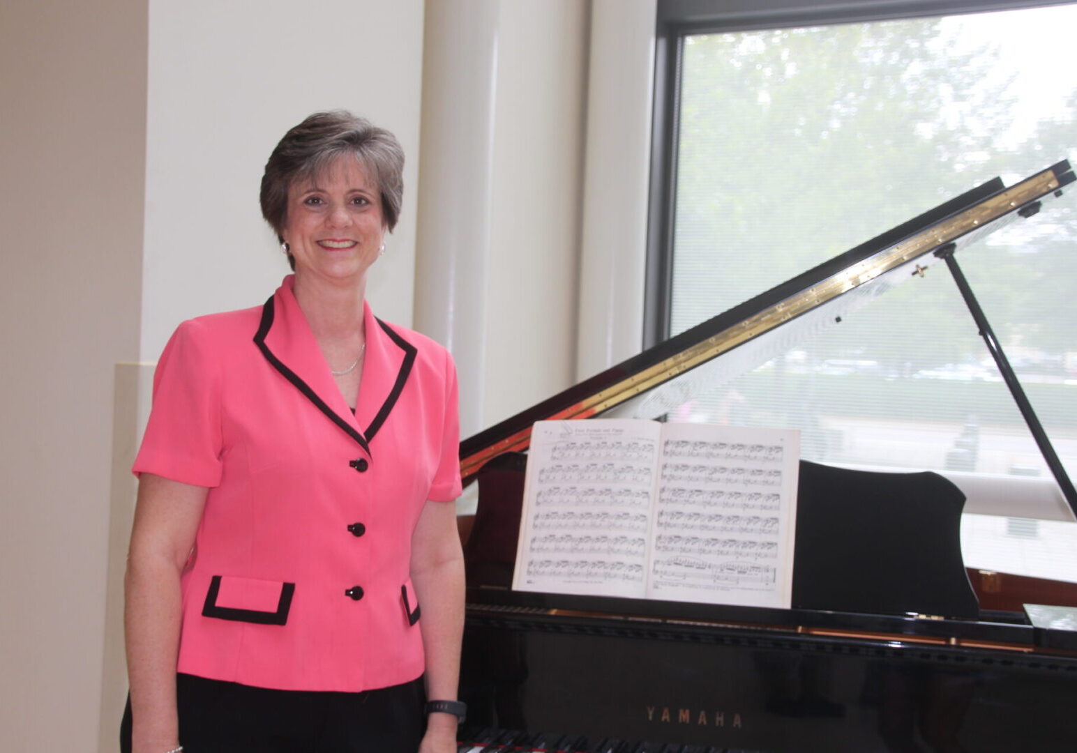 A woman standing next to a piano in front of a window.